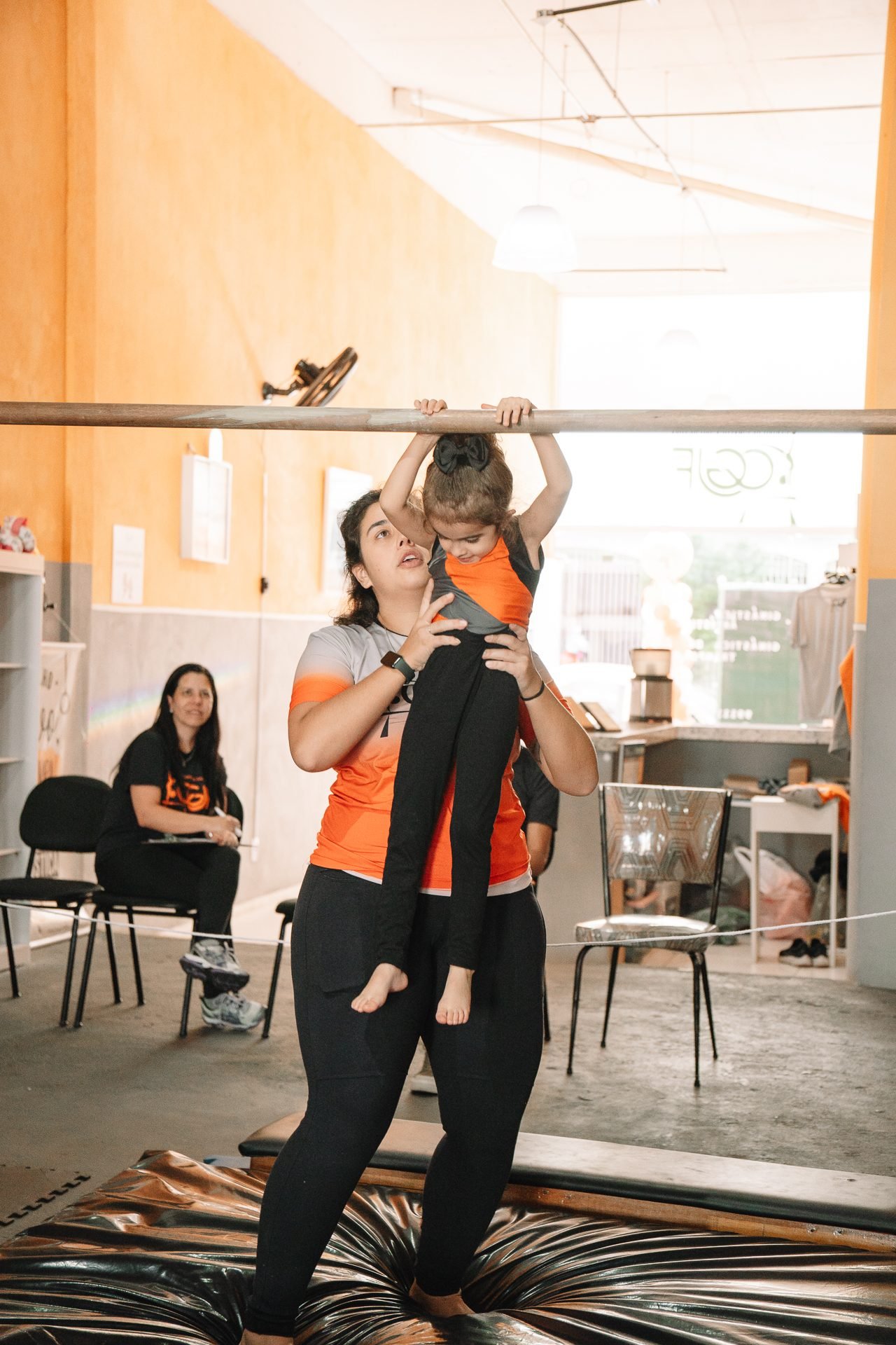 Criança pequena treinando na barra com apoio da professora